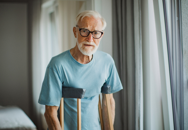 Portrait of an elderly man with crutches at home.