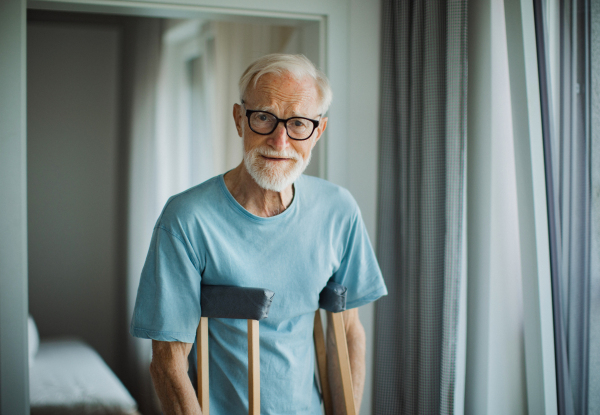 Portrait of an elderly man with crutches at home.