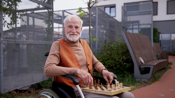 Close up of senior man playing chess outdoors alone. Nursing home client, enjoying a game of solitaire chess, chess puzzle.