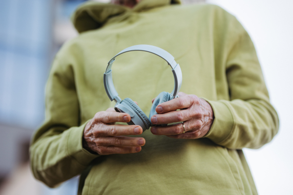 Close up of elderly man holding wireless headphones, listening to music while exercising outdoors.