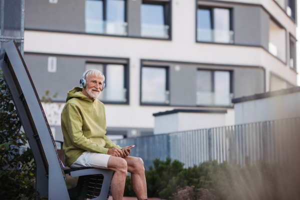 Senior man exercising outdoors in the city. Elderly man resting on a bench, listening to music through wireless headphones, preparing for his morning run.