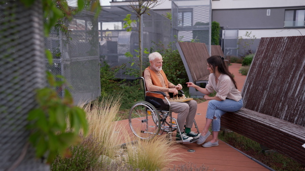 Senior man playing chess outdoors with his daughter. Nursing home client in wheelchair spending quality time with caregiver, enjoying in a game of chess and conversation.