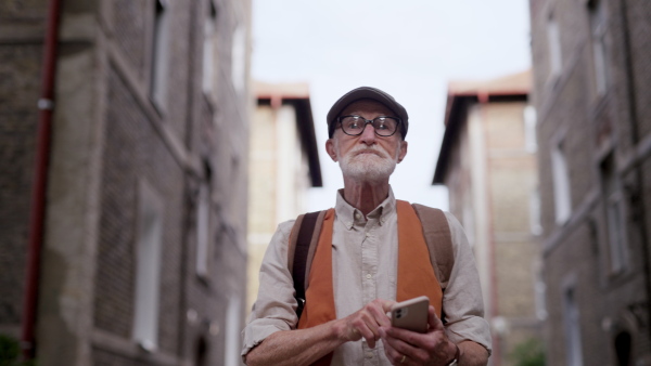 Senior tourist exploring a new city and visiting interesting sites. Elderly man strolling through the city while holding a smartphone.