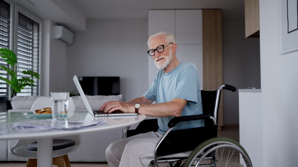 Senior man in a wheelchair working from home during retirement. Video of elderly man using digital technologies, working on a laptop. Concept of seniors and digital skills.