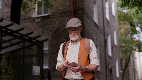 Senior tourist exploring a new city and visiting interesting sites. Elderly man strolling through the city while holding a smartphone.