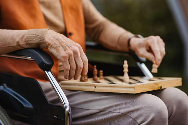 Close up of senior man playing chess outdoors alone. Nursing home client, enjoying a game of solitaire chess, chess puzzle.