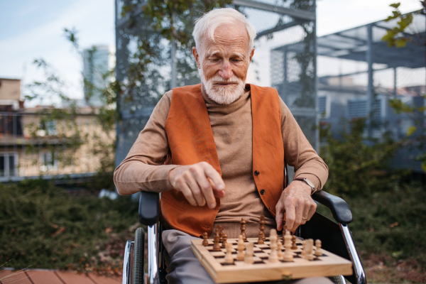 Senior man playing chess outdoors alone. Nursing home client, enjoying a game of solitaire chess, chess puzzle.