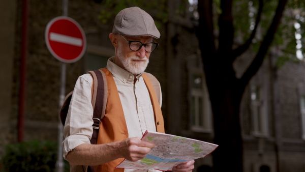 Senior tourist exploring a new city, exploring interesting places. Elderly man holding a paper map and looking for the route. Traveling and trips in retirement.