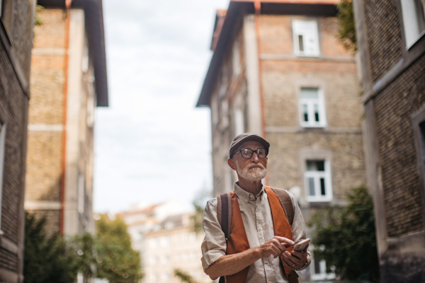 Senior tourist exploring a new city and visiting interesting sites. Elderly man strolling through the city while holding a smartphone.