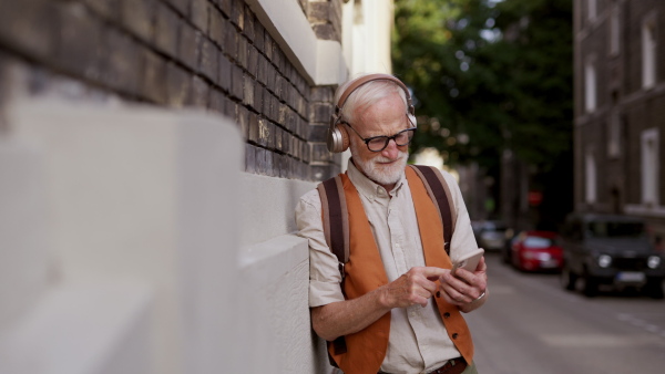 Close up shot of a senior man on the street. Elderly cool man listening to music outdoors, having fun. Concept of old man young at heart.