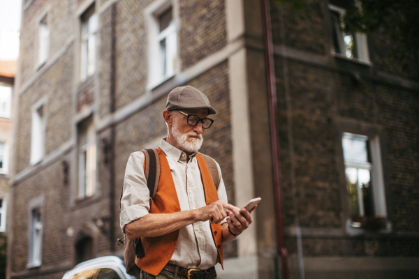 Senior tourist exploring a new city and visiting interesting sites. Elderly man strolling through the city while holding a smartphone.