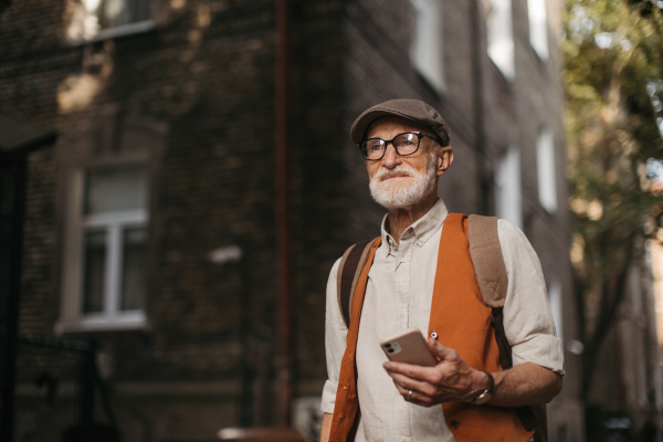 Senior tourist exploring a new city and visiting interesting sites. Elderly man strolling through the city while holding a smartphone.