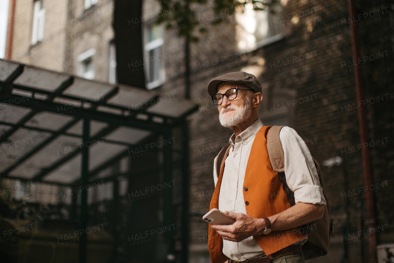 Senior tourist exploring a new city and visiting interesting sites. Elderly man strolling through the city while holding a smartphone.