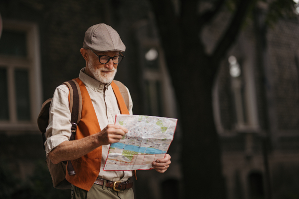 Senior tourist exploring a new city, exploring interesting places. Elderly man holding a paper map and looking for the route. Traveling and trips in retirement.