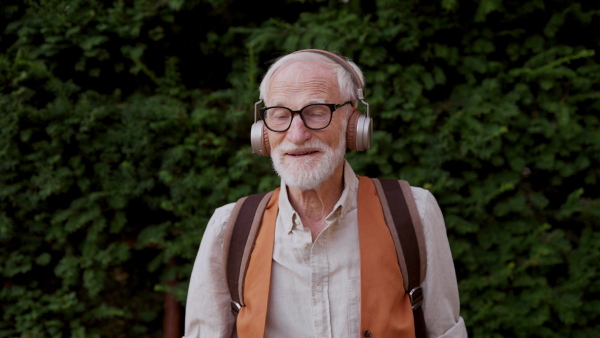 Video of a senior man on the street with hands in pockets. Elderly cool man listening to music outdoors, having fun. Concept of old man young at heart.