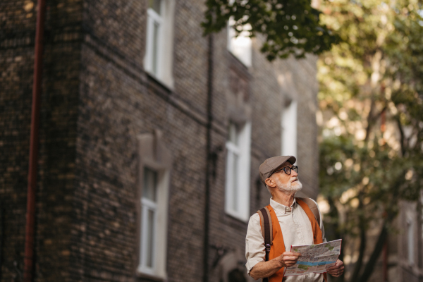 Senior tourist exploring a new city, exploring interesting places. Elderly man holding a paper map and looking for the route. Traveling and trips in retirement.