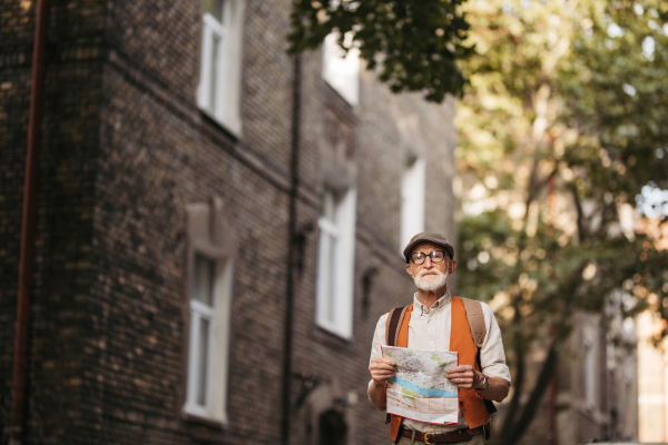 Senior tourist exploring a new city, exploring interesting places. Elderly man holding a paper map and looking for the route. Traveling and trips in retirement.