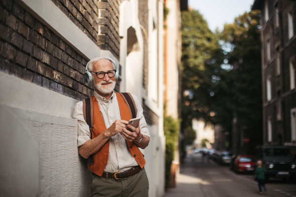 Close up shot of a senior man on the street. Elderly cool man listening to music outdoors, having fun. Concept of old man young at heart.