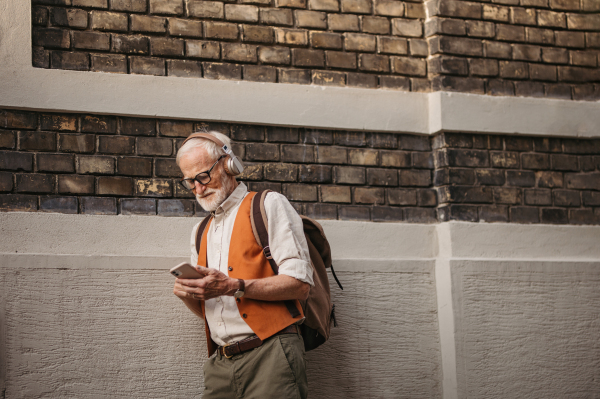 Close up shot of a senior man on the street. Elderly cool man listening to music outdoors, having fun. Concept of old man young at heart.