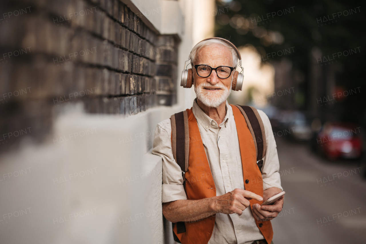 Close up shot of a senior man on the street. Elderly cool man listening to music outdoors, having fun. Concept of old man young at heart.