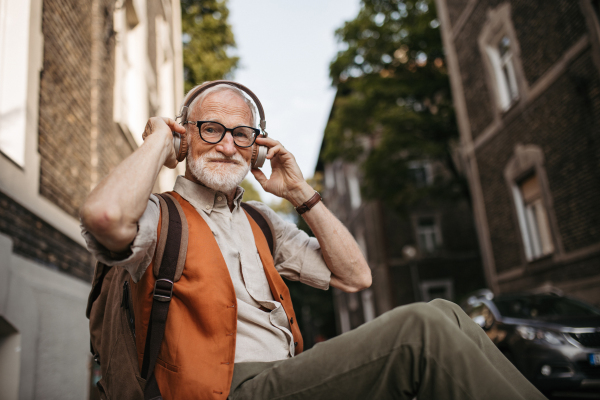 Close up shot of a senior man on the street. Elderly cool man listening to music outdoors, having fun. Concept of old man young at heart.