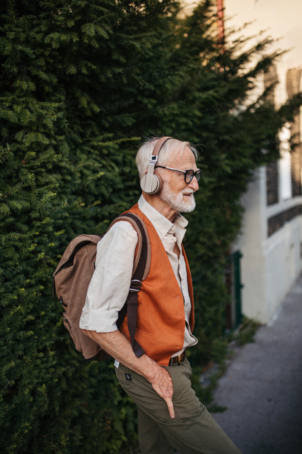 Portrait of a senior man on the street with hands in pockets. Elderly cool man listening to music outdoors, having fun. Concept of old man young at heart.