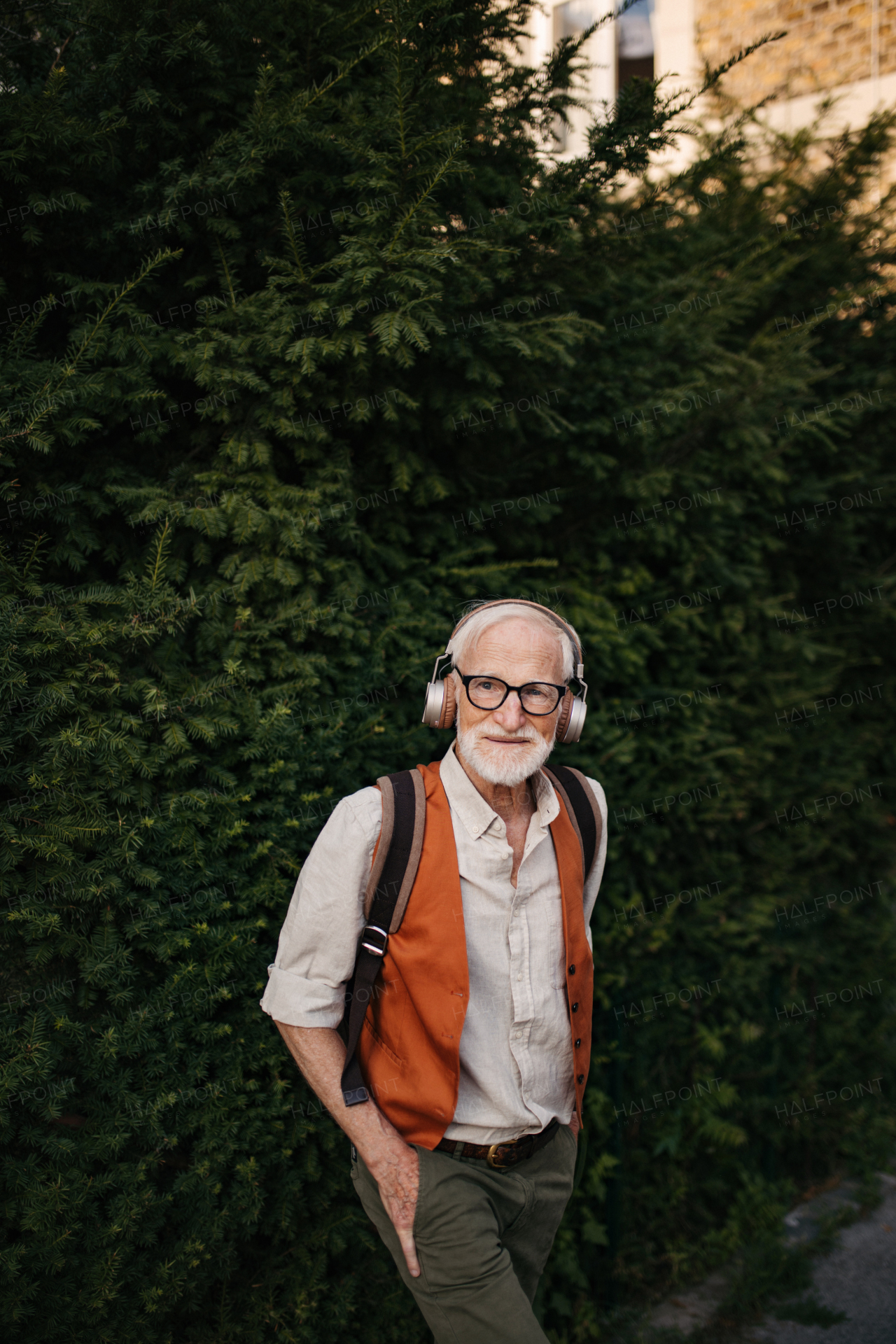 Portrait of a senior man on the street with hands in pockets. Elderly cool man listening to music outdoors, having fun. Concept of old man young at heart.