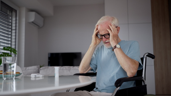 Portrait of senior man in wheelchair taking pills at home, he is confused about mediacation usage. Chronically ill man have no money for his medication.