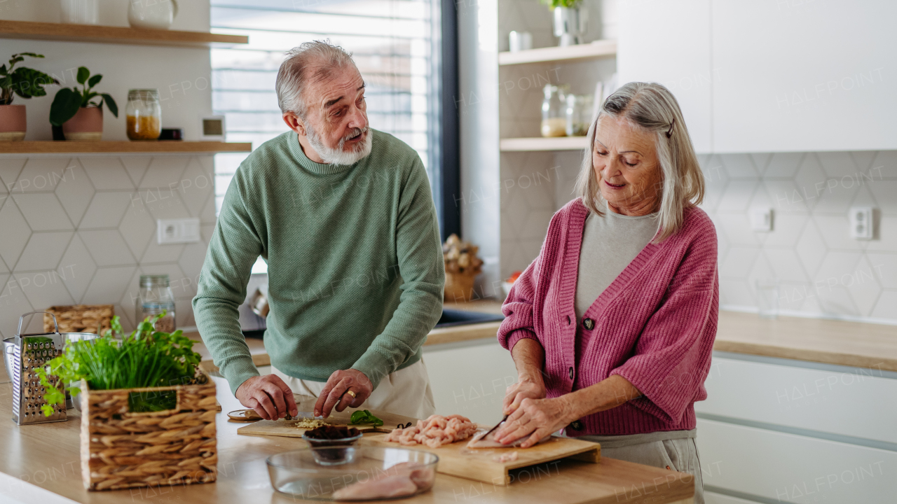 Senior couple cooking together in the kitchen, preparing chicken for dinner. Spending quality time together.