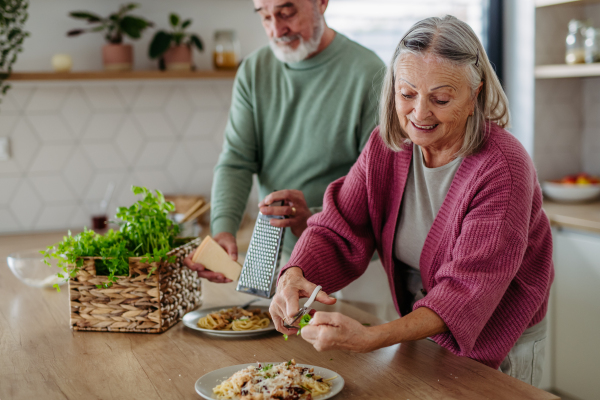 Senior couple cooking together in the kitchen, preparing pasta for dinner. Spending quality time together.