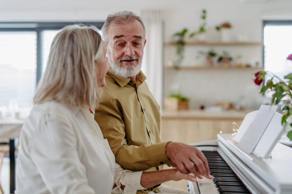 A senior couple sitting side by side at the piano, playing together.