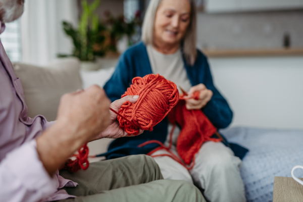 Senior couple knitting together in the living room. Husband helps to wind yarn.