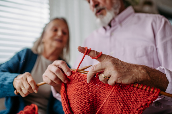 Senior couple knitting together in the living room. An elderly man is learning to knit.