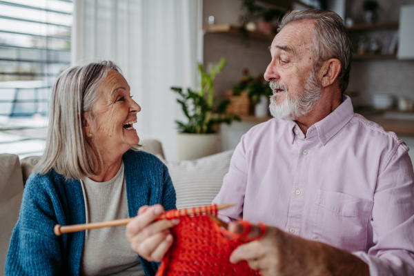 Senior couple knitting together in the living room.