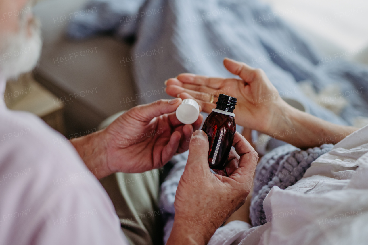 Close up of senior man giving pills to his ill wife. Taking prescribed medication.