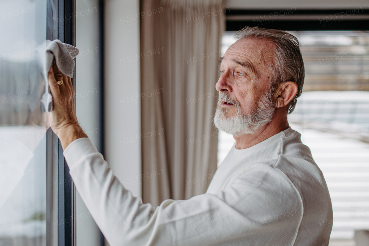 Senior man cleaning windows in his apartment..