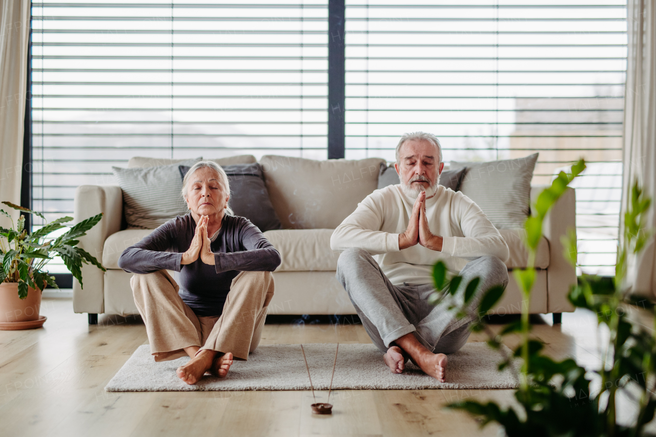 Senior couple is doing yoga together in living room. Healthy lifestyle concept.