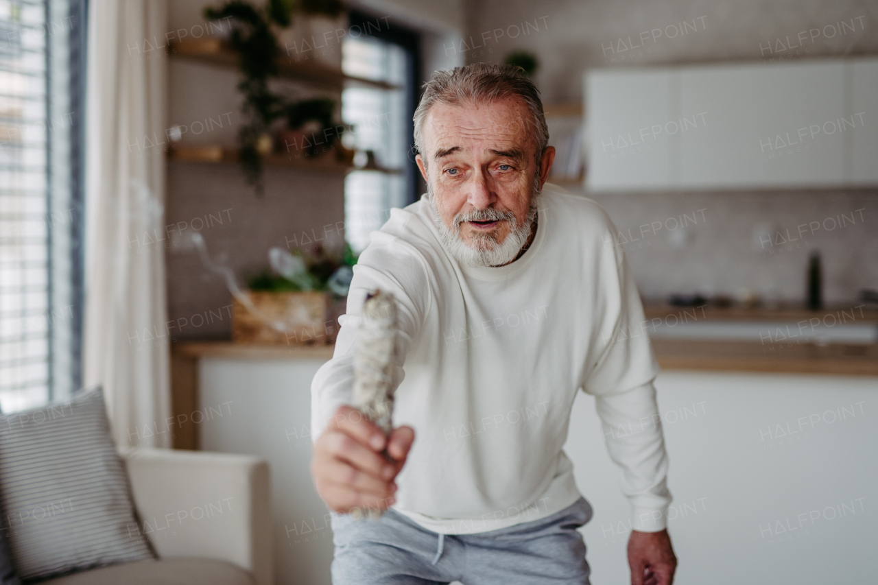 Senior man doing ritual with a sage in his home.