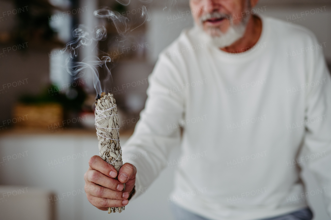 Senior man doing ritual with a sage in his home.