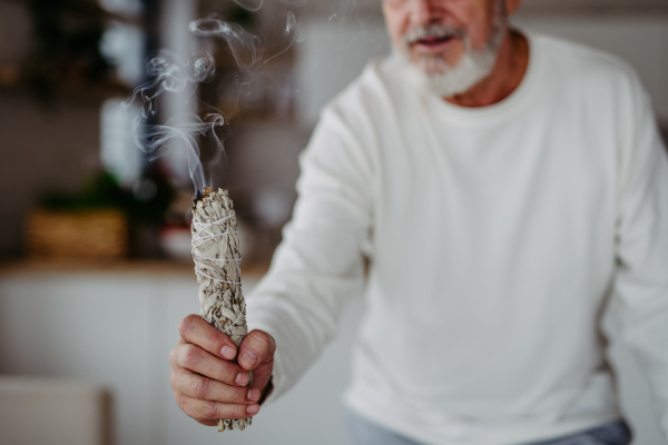 Senior man doing ritual with a sage in his home.