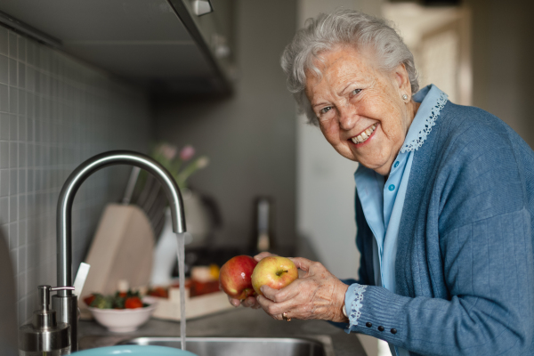 Happy senior woman washing apples in the kitchen.