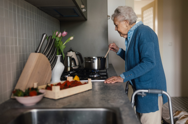 Happy senior woman cooking in the kitchen. Gradmother making jam from fresh strawberries.