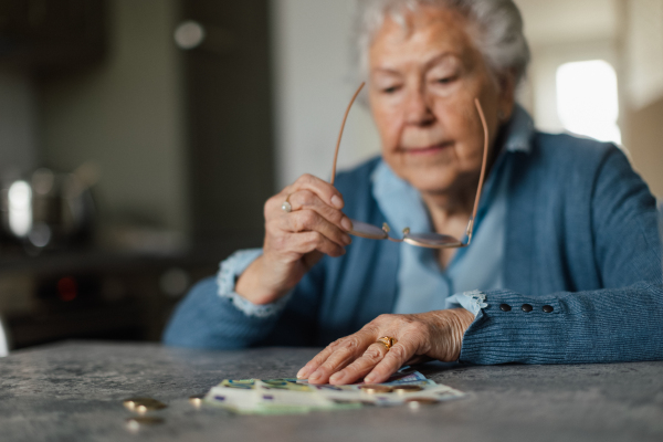 Unhappy senior woman counting her pension at home. Financial issues of the eldery.