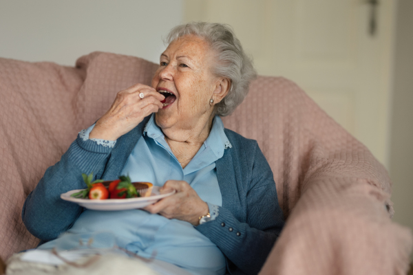 Senior woman resting at her home and eating strawberries.