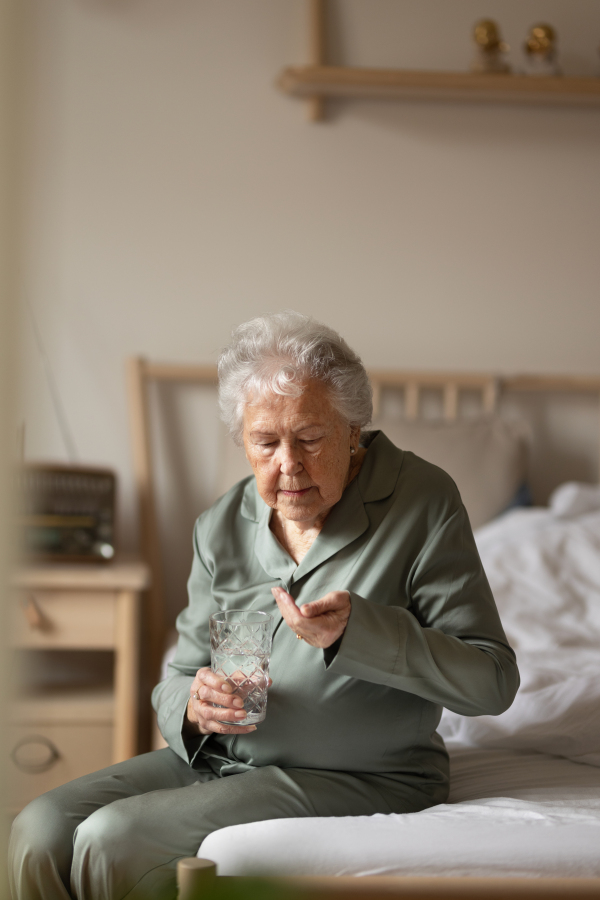 Senior woman sitting on her bed and taking pills.