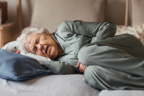 Senior woman sleeping in her bed alone. Woman having pain a feeling anxious. Loneliness and social isolation of eldery woman.