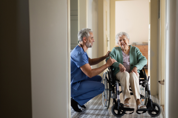 Caregiver doing regular check-up of senior client in her home. Thoughful male nurse taking care of eldery patient on wheelchair.