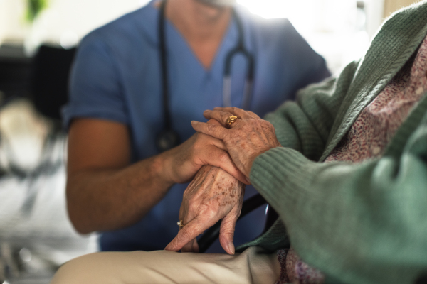 Close up of caregiverr holding hands of his senior client, concept of healthcare and relationships.