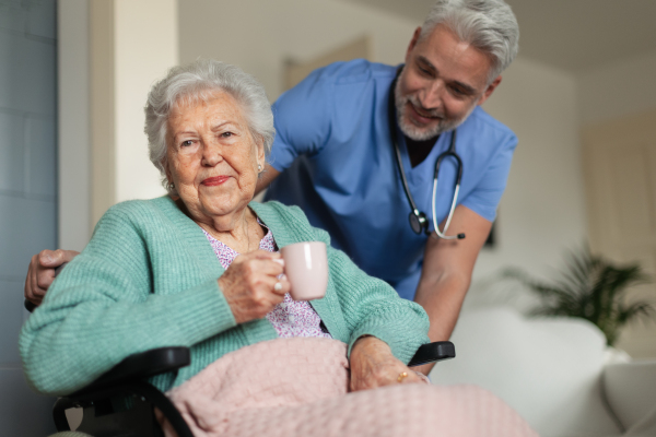 Caregiver doing regular check-up of senior client in her home. Thoughful male nurse taking care of eldery patient on wheelchair.