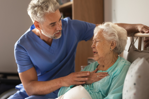 Doctor helping senior patient with chest pain. Thoughful male nurse taking care of eldery patient struggling with breathing.